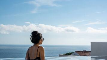 A person in a black swimsuit standing in a pool with a view of the sea and a building in the background.