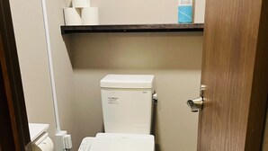 Un baño pequeño con inodoro blanco, dispensador de toallas de papel y dispensador de jabón sobre una repisa.