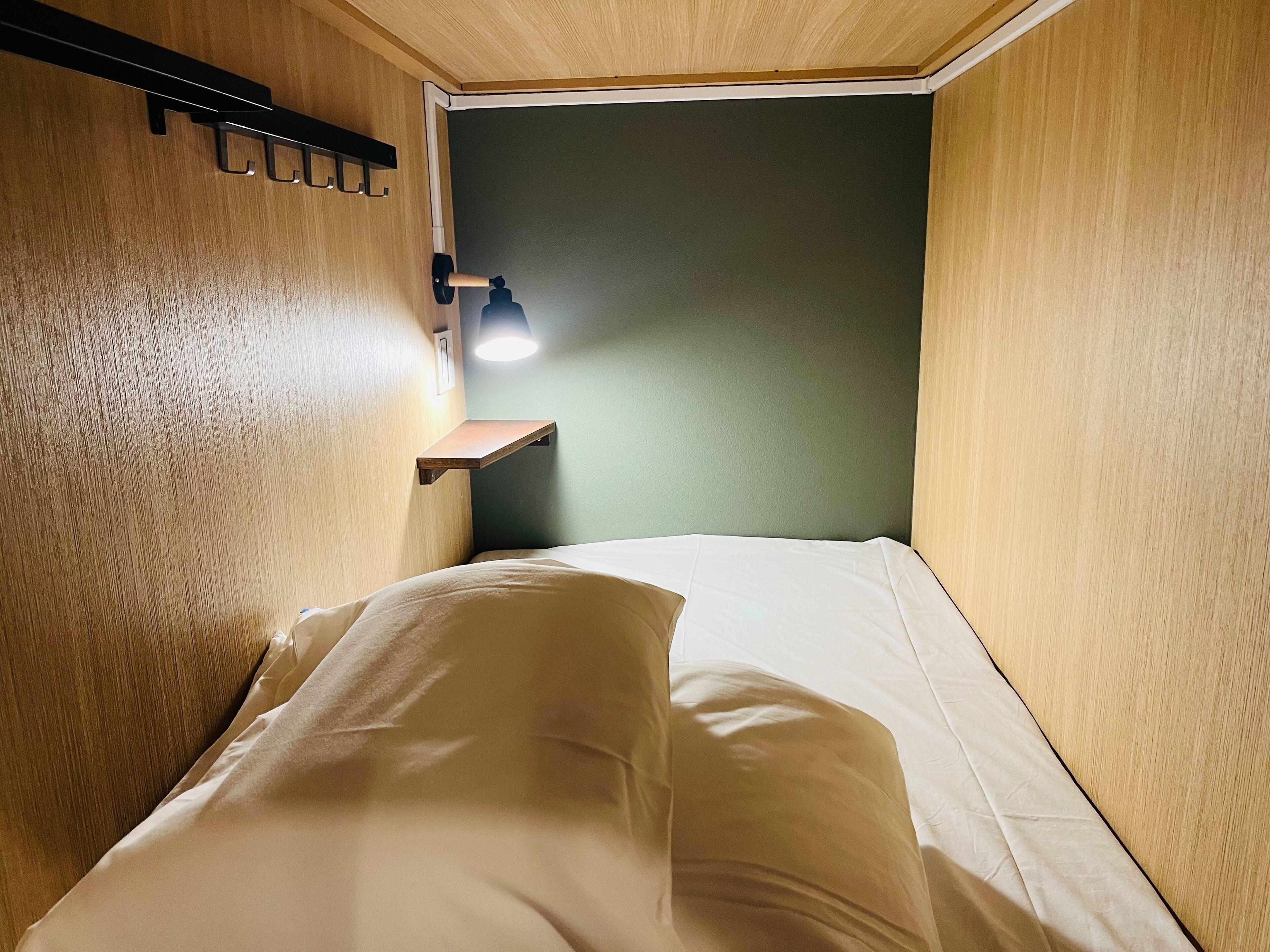 Ein kleines, gemütliches Zimmer mit einem Bett, einem Wandregal und einer Nachttischlampe.