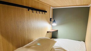 Una habitación pequeña y acogedora con cama, cabecero de madera, estante en la pared y lámpara de noche.
