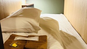 Una habitación pequeña con una cama individual, cabecera de madera, una mesita de noche y un buró.