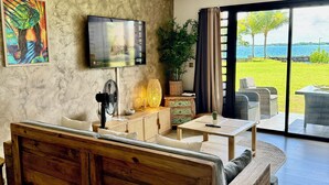 A modern living room with a wooden sofa, a television, a large window with a view of the sea, and a wicker lamp. - Bora Bora, Otemanu lagoon F2 with lagoon view (Anau bora bora)