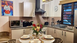 A modern kitchen with white cabinets, a central island with a vase of flowers, and a dining area with wicker chairs and a round table set for four. - Bora Bora, Otemanu lagoon F2 with lagoon view (Anau bora bora)