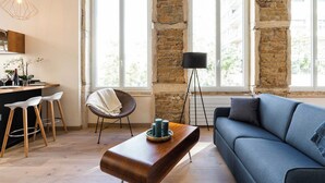 Ein modernes Wohnzimmer mit Steinwand, blauem Sofa, Couchtisch aus Holz und einer schwarzen Stehlampe.