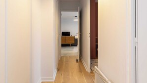 A narrow hallway with wooden flooring leading to a room with a bed and a dresser.