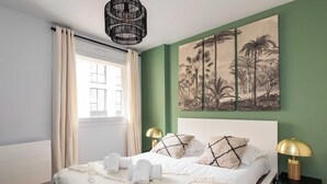 A bedroom with a bed, two bedside lamps, a wall-mounted artwork, and a window with curtains.
