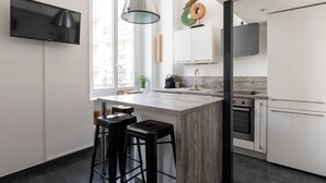 A modern kitchen with a large island, bar stools, a built-in oven, and a hanging light fixture. - DIFY Boileau - Quartier Foch (Lyon)