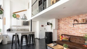 A modern kitchen with a central island, black bar stools, a wooden coffee table, and a brick-patterned wall. - DIFY Boileau - Quartier Foch (Lyon)