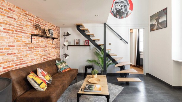 A modern living room with a brick wall, a brown leather sofa, a wooden coffee table, and a staircase with a black railing. - DIFY Boileau - Quartier Foch (Lyon)