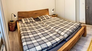 A bedroom with a wooden bed, plaid bedding, two bedside lamps, a wooden nightstand, and a wall-mounted decoration. - Apartment BD-D by Interhome (Bozi Dar)