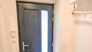 A hallway with a dark door, a bench, a coat rack, and a small table with a bowl. - Apartment BD-D by Interhome (Bozi Dar)