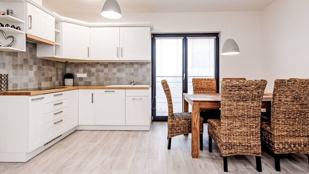 A modern kitchen with white cabinets, a wooden countertop, and a dining area with wicker chairs and a wooden table. - Apartment Ness by Interhome (Bozi Dar)
