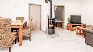 A modern living room with a fireplace, a dining area with wicker furniture, and a television on a wooden stand. - Apartment Ness by Interhome (Bozi Dar)