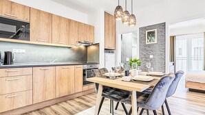 Une cuisine moderne avec des meubles en bois, un four encastré et un coin repas avec une table dressée pour quatre personnes.