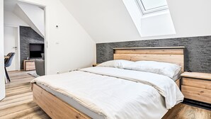 Une chambre moderne avec un plafond en pente, un puits de lumière, un lit en bois, une table de chevet et un téléviseur fixé au mur.