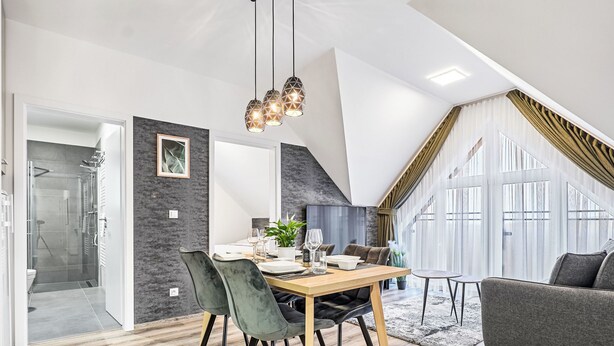 Un espace de repas moderne avec une table et des chaises en bois, un lustre et une vue sur l’extérieur.