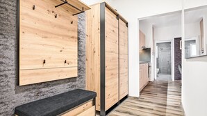 Un intérieur moderne avec un meuble mural en bois, un banc et un coin cuisine visible à travers une porte ouverte.