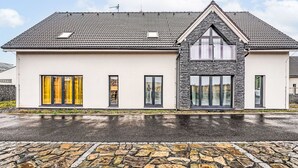 Moderni, kaksikerroksinen talo, jossa on kiviverhous, suuret ikkunat ja laattakatto.
