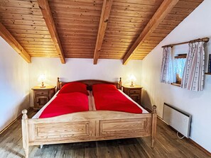 A wooden bed with a red blanket in a room with wooden beams on the ceiling and two bedside tables with lamps.