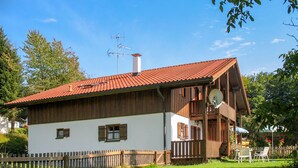 A wooden house with a red-tiled roof, a balcony, and a fenced yard.