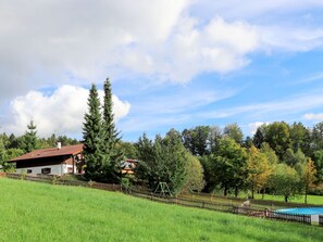 A house with a red roof, surrounded by a wooden fence and a grassy field.