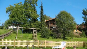 A swimming pool with a wooden deck, a swing set, and a fenced area.