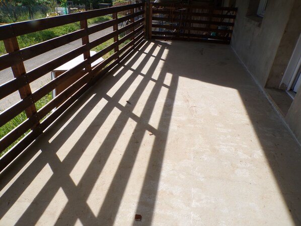 Un balcón con baranda de madera, piso de concreto y vistas a la vegetación.
