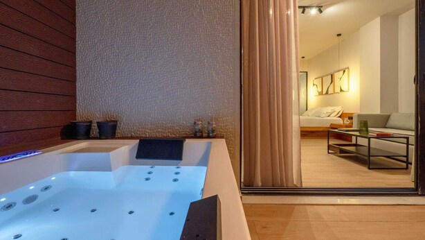 Un baño moderno con bañera, paneles de madera y un espejo que refleja una sala de estar con sofá y mesa de centro.