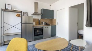 A compact kitchen with modern appliances, a dining area with a yellow chair, and a small table. - DIFY Wilson - Villeurbanne (Villeurbanne)