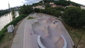 A skate park with a curved ramp and a circular bowl, surrounded by a paved walkway and greenery. - DIFY Wilson - Villeurbanne (Villeurbanne)