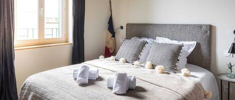 A neatly made bed with towels, a hanging lamp, and a view of the outside through a window.