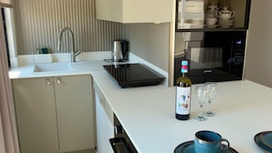 Une cuisine moderne équipée d’un four encastré, d’un micro-ondes et d’une bouteille de vin posée sur le plan de travail.