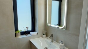 Une salle de bain moderne avec une fenêtre intégrée, un grand miroir et un lavabo blanc.