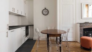 Een moderne keuken met witte kasten, een houten eettafel met transparante stoelen en een klok aan de muur.