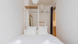 A neatly made bed with white linens and towels, a wooden headboard, a white wall, and a door leading to another room. - DIFY Lovely - Centre-ville (Lyon)