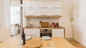 A modern kitchen with white cabinets, a wooden countertop, and a dining area with a table set for two. - DIFY Lovely - Centre-ville (Lyon)