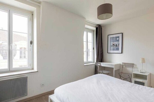 A bedroom with a bed, a window, a radiator, a desk, and a chair.