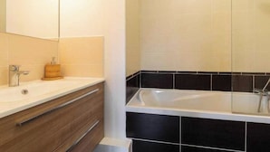 A modern bathroom with a large mirror, a white sink, a wooden vanity, and a black-tiled shower area. - DIFY Palais - Cordeliers (Lyon)