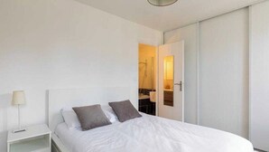 A bedroom with a bed, two pillows, a nightstand, a lamp, and a sliding door to a bathroom. - DIFY Palais - Cordeliers (Lyon)