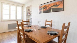 A dining area with a wooden table set for four, surrounded by wooden chairs. There is a bookshelf with books and a framed picture on the wall. - DIFY Palais - Cordeliers (Lyon)