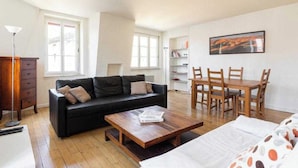 A modern living room with a black sofa, wooden coffee table, and a dining area with wooden chairs and a table. - DIFY Palais - Cordeliers (Lyon)