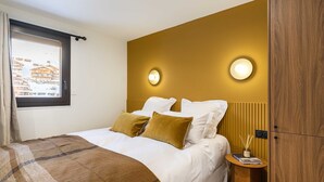 Een hotelkamer met een bed, twee nachtkastjes, een raam met uitzicht op gebouwen en een muur met twee wandlampen.