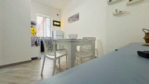 A modern kitchen with white cabinetry, a dining area with white chairs, and a view of the city through a window. - That's Amuri - Holiday apartment (Palermo)