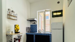 A compact kitchen with a white refrigerator, a coffee machine, and a small cart with cups. - That's Amuri - Holiday apartment (Palermo)