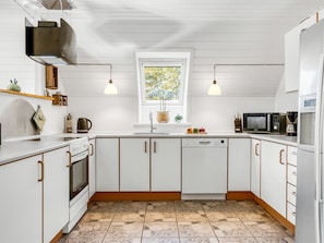A modern kitchen with white cabinetry, a dishwasher, a stove, a microwave, and a refrigerator. There is a window with a view of greenery outside.