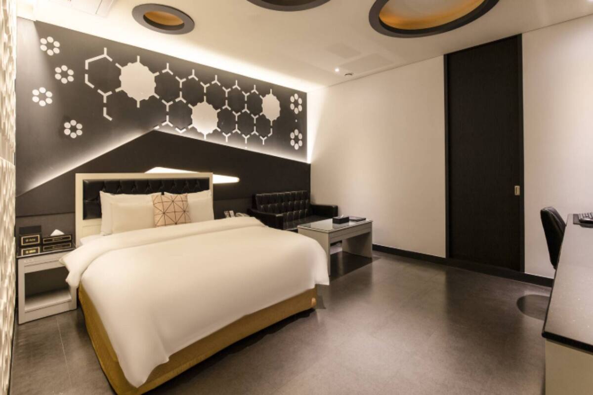 Ein modernes Hotelzimmer mit einem großen Bett, einem Nachttisch, einer Couch und einem Schreibtisch mit Stuhl.