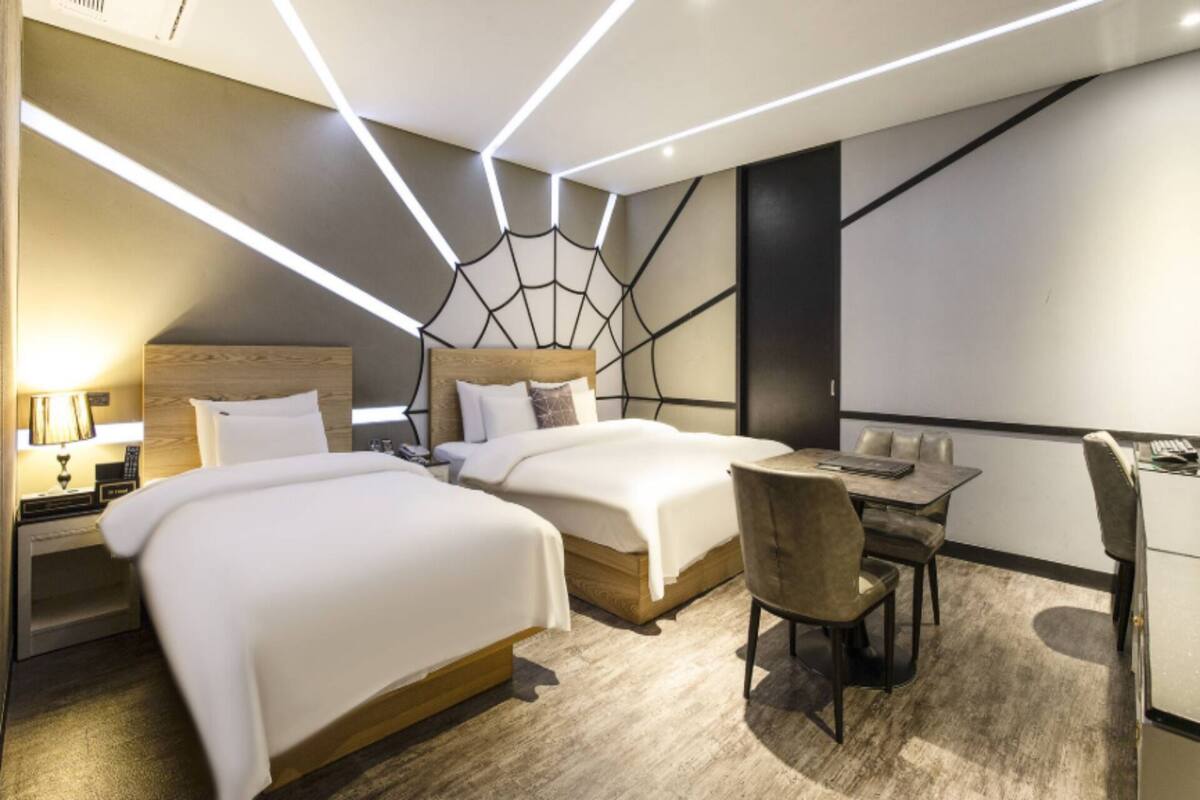 Ein modernes Hotelzimmer mit zwei Betten, einem Schreibtisch und einem Stuhl.