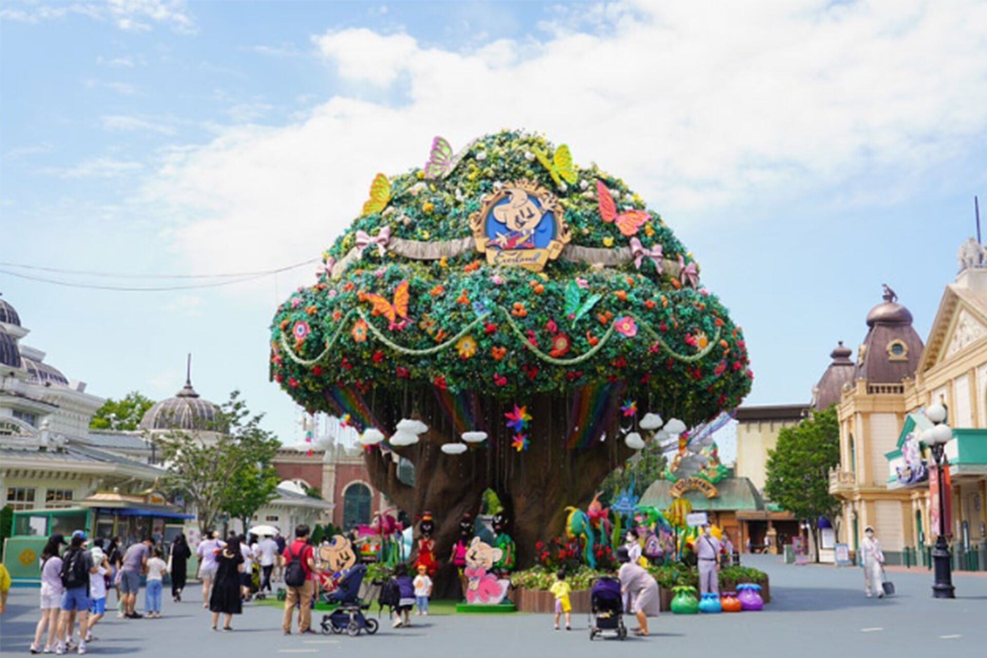 Un grand arbre décoré de façon élaborée, avec une pancarte indiquant « Disneyland » à sa base, entouré d’une foule de personnes.