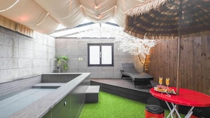 A modern spa area with a stone wall, a small window, a thatched roof, a red table with drinks, and a green artificial turf. - 3S HOTEL DONGTAN - BOUTIQUE (Hwaseong)