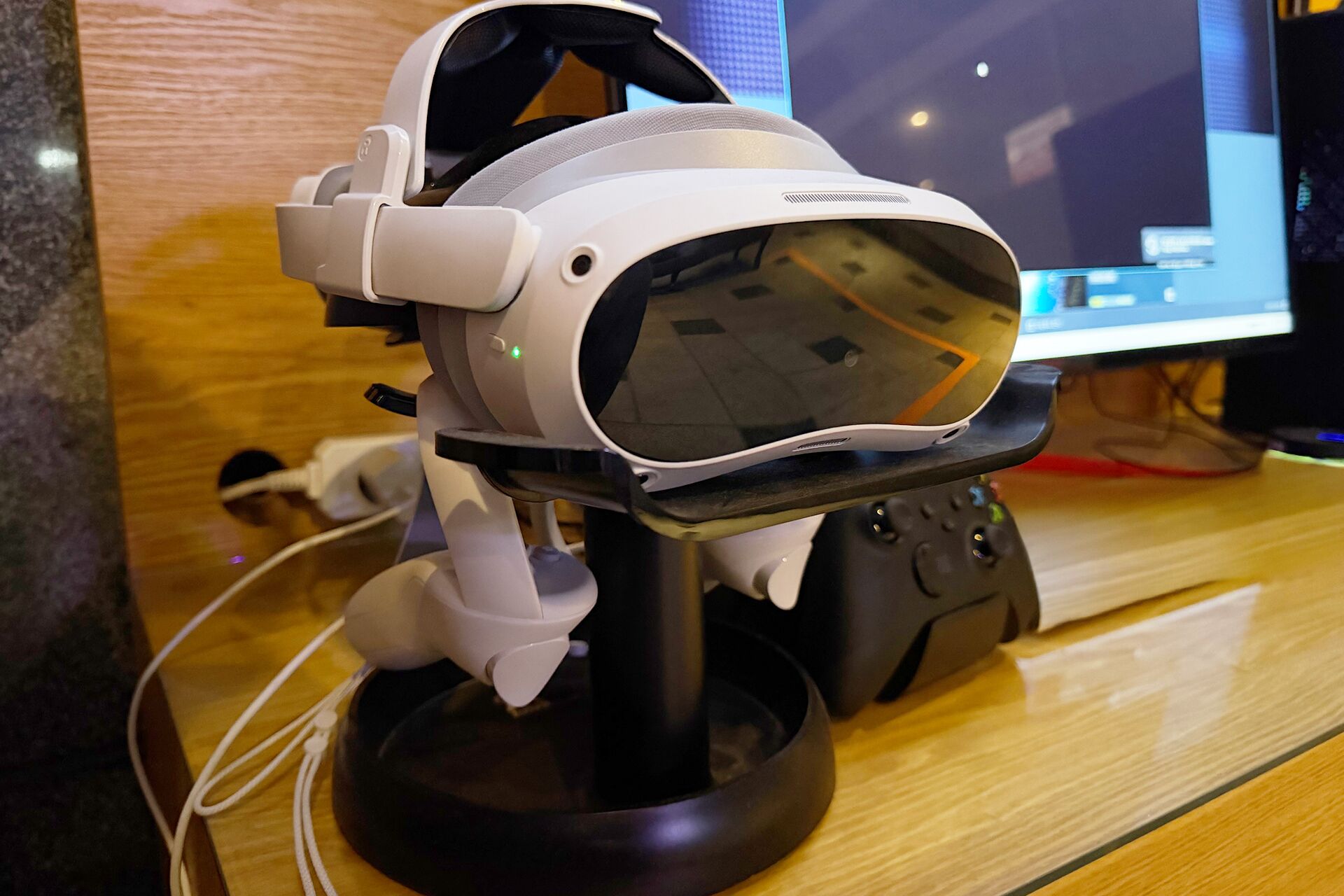 Un visor de realidad virtual sobre un soporte, con un monitor de computadora al fondo.